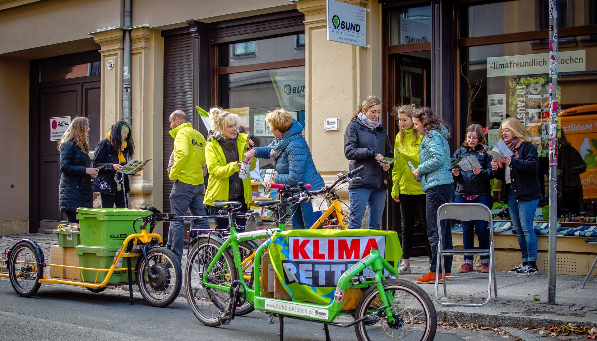 Menschen stehen vor dem Büro des BUND Dresden und unterhalten sich. Sie tragen gelbe Regenjacken.