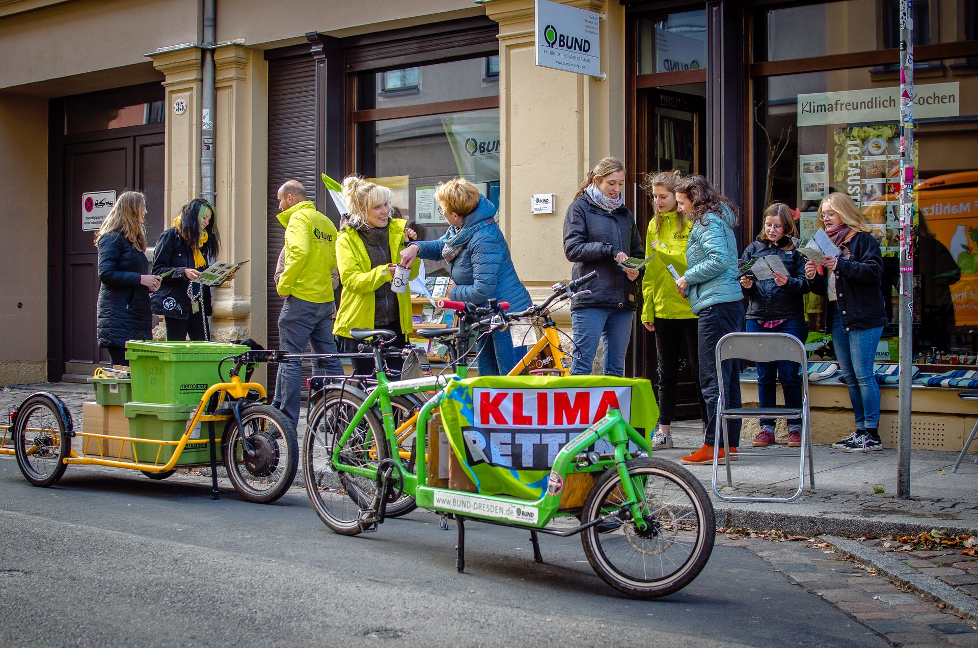 Menschen stehen vor dem Büro des BUND Dresden und unterhalten sich. Sie tragen gelbe Regenjacken.