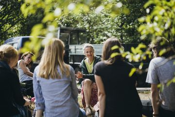Menschen sitzen in einem Stuhlkreis zusammen und hören einer Frau zu.