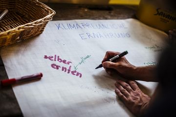 Hand schreibt mit Filzstift eine Art Mindmap auf großes Papier. Darauf steht: Klimafreundliche Ernährung. Selber anpflanzen, anbauen. 