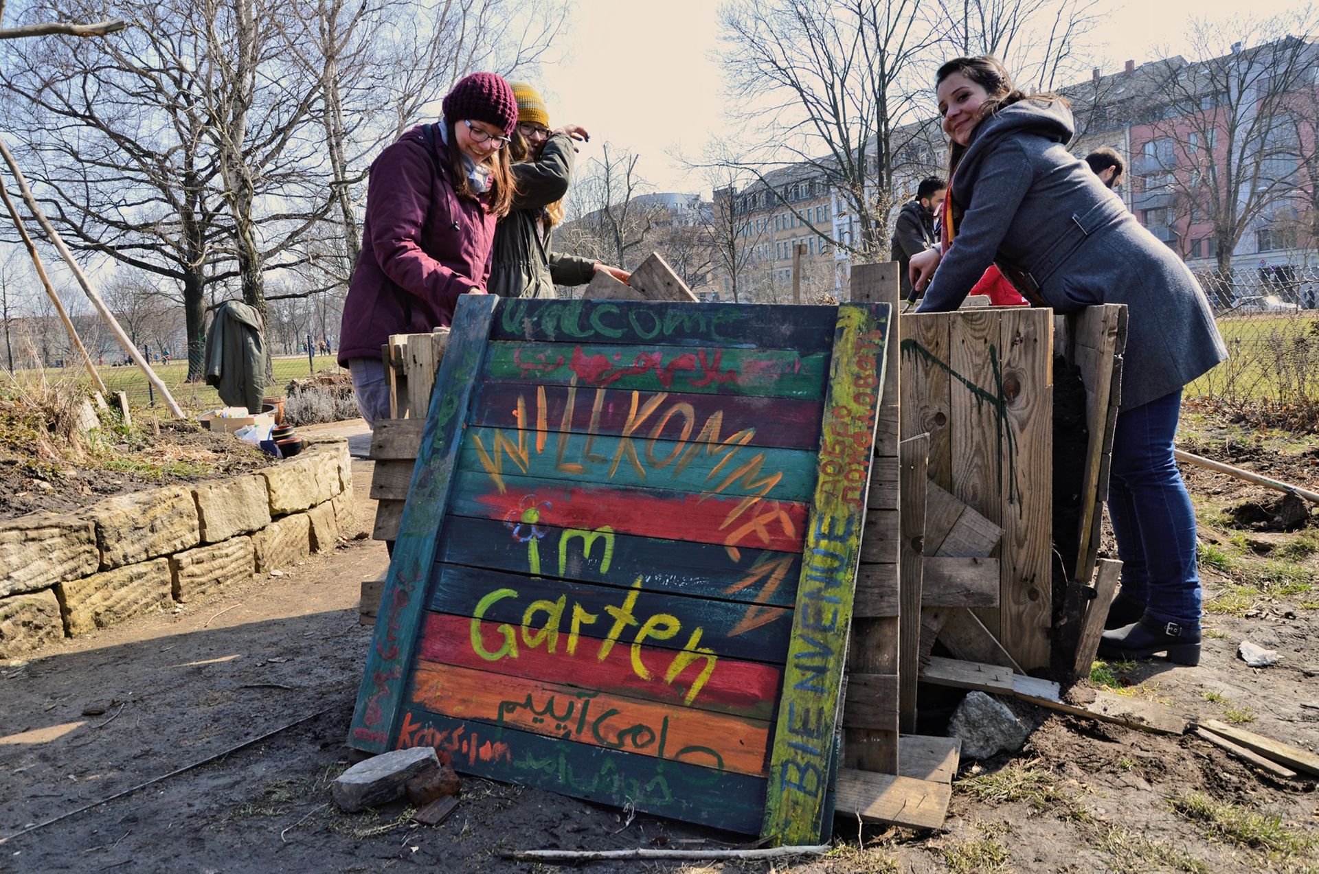 Vier Personen stehen vor einem bunten Schild, auf dem steht: Willkommen im Garten