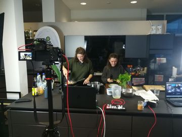 Zwei Frauen, die in der Küche arbeiten, vor ihnen stehen Kameras.