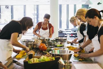 Die Teilnehmer:innen des Kochkurses stehen an einer Kücheninsel und schneiden Gemüse. 