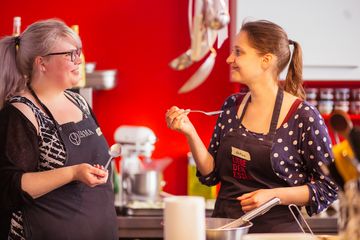 Zwei Frauen schmecken mit Löffeln das Essen ab.