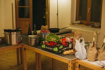 Ein Pappkarton mit frischem Gemüse und zwei Weinflaschen stehen auf einem Tisch.