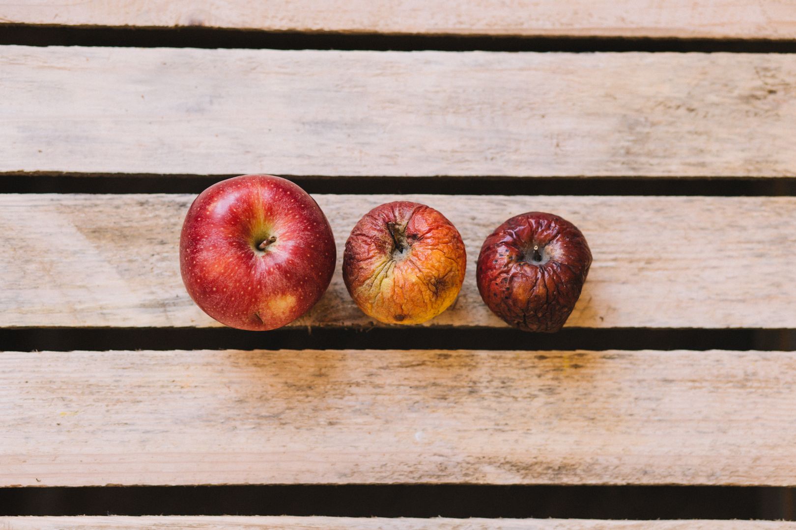 Three red apples of different sizes lying on wood.