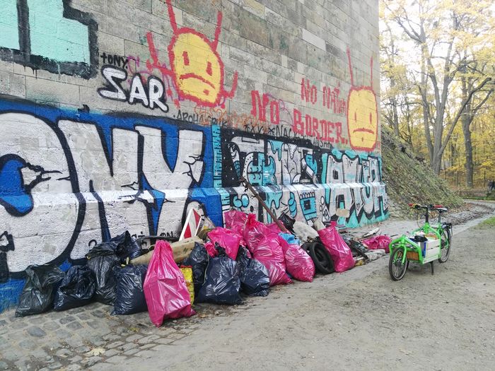 Das grüne Lastenrad und volle Müllbeutel neben einer mit Graffitti besprühten Wand.