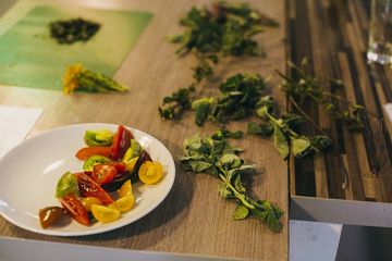 Ein Teller mit geschnittenen Tomaten steht auf einem Tisch, daneben liegen Kräuter.
