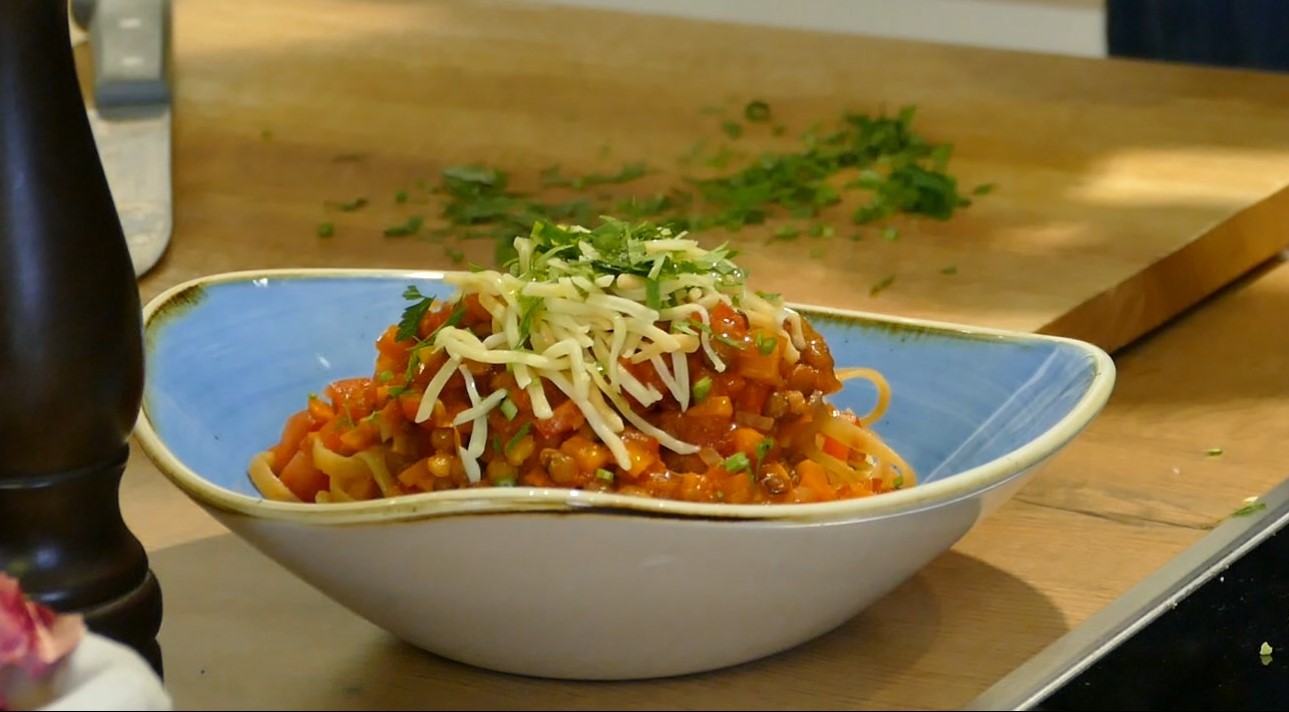 Lentil bolognese is sprinkled with cheese and served on a plate on a wooden table.