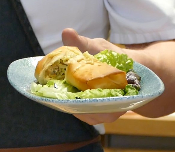 Vegetable strudel and salad are arranged on a small patterned plate held up to the camera by a person.