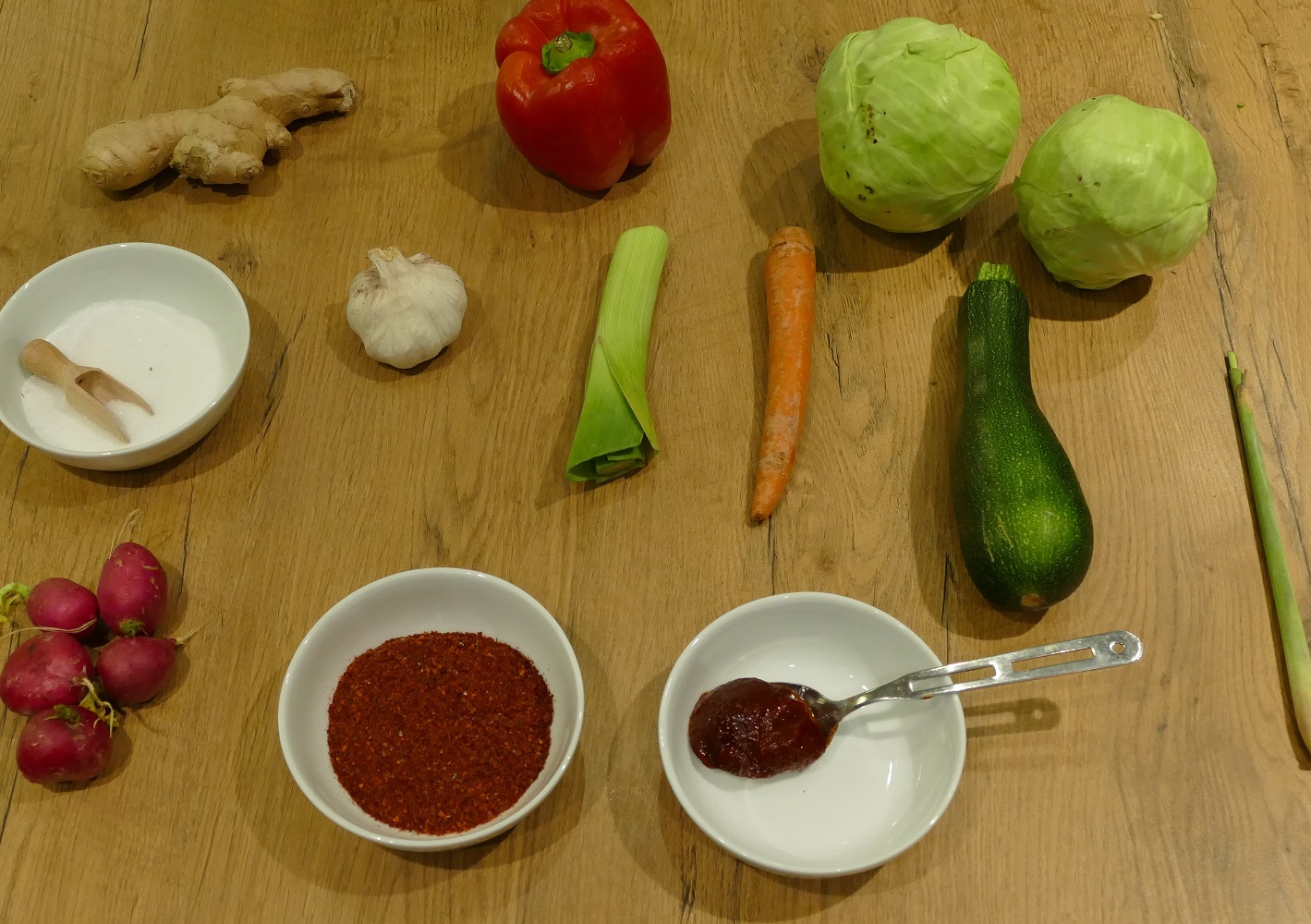 Zutaten wie Porree, Zucchini, Paprika, Möhre oder Knoblauch liegen auf einem Holztisch.