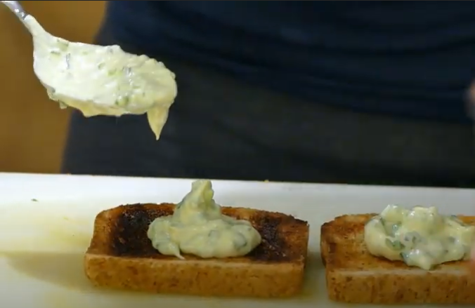 Helle Creme wird auf Toastscheiben angerichtet, welche auf einer große, weißen Platte liegen.