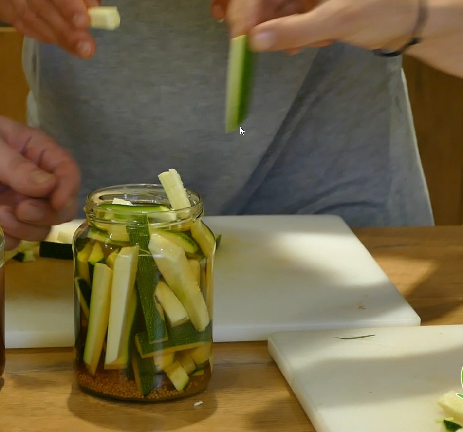 Courgette strips are taken out of a preserving jar by a person in a grey T-shirt.