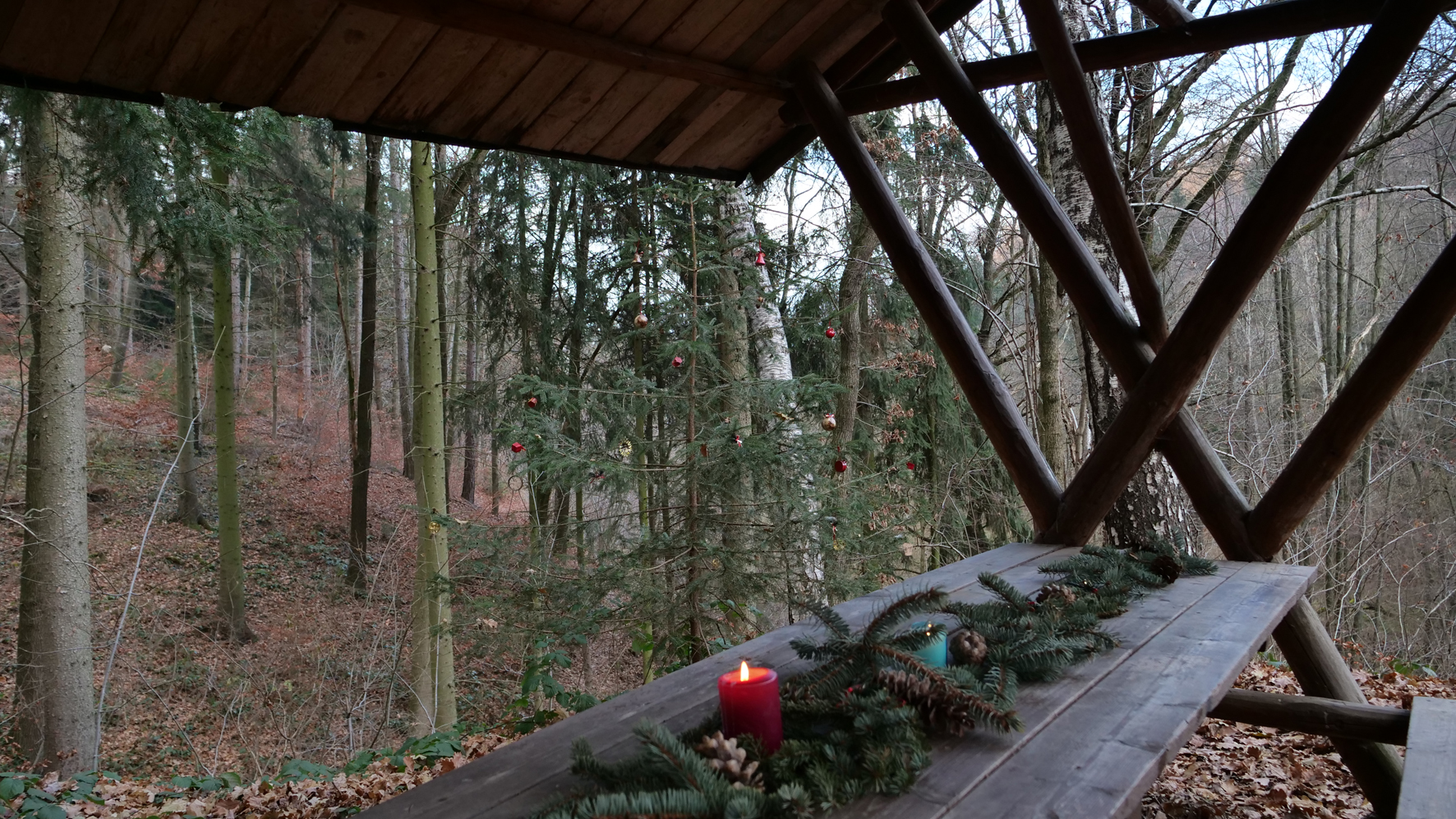 Überdachter Tisch im Wald, der mit Nadelzweigen und einer roten, brennenden Kerze geschmückt ist.