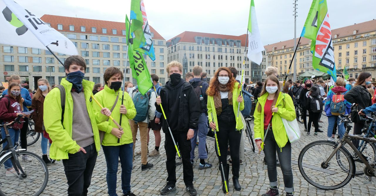 Fünf Mitglieder der BUNDjugend beim Klimastreik auf dem Altmarkt. Sie tragen Masken, die meisten von ihnen eine neonfarbene BUND-Jacke und zwei Fahnen, auf denen steht: Klima retten!