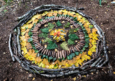 Mandala aus verschiedenen Naturmaterialien, wie Stöcke, bunte Blätter, Tannenzapfen oder Farnwedel. 